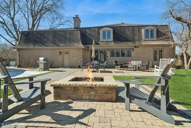 rear view of house with brick siding, an outdoor living space with a fire pit, a patio, and a shingled roof