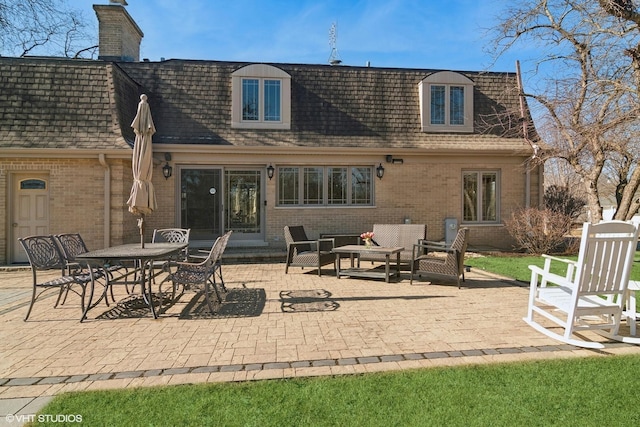 back of property featuring a patio, a chimney, brick siding, and a shingled roof