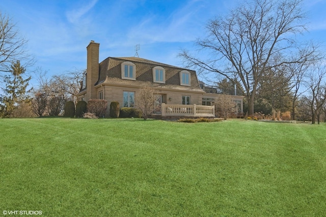 rear view of house featuring a lawn, a deck, mansard roof, a shingled roof, and a chimney