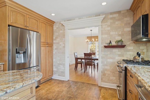 kitchen featuring light wood finished floors, light stone countertops, a chandelier, ornamental molding, and stainless steel appliances