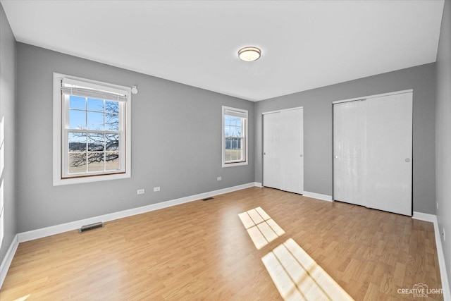 unfurnished bedroom featuring wood finished floors, visible vents, two closets, and baseboards