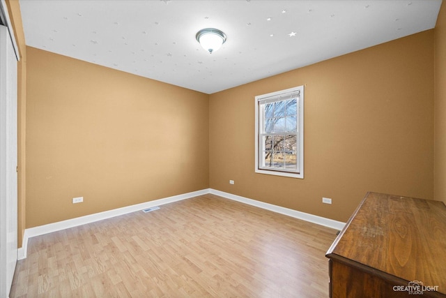 spare room with light wood finished floors, visible vents, and baseboards