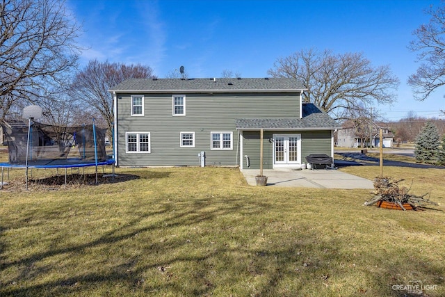 back of property featuring a shingled roof, a trampoline, french doors, a yard, and a patio