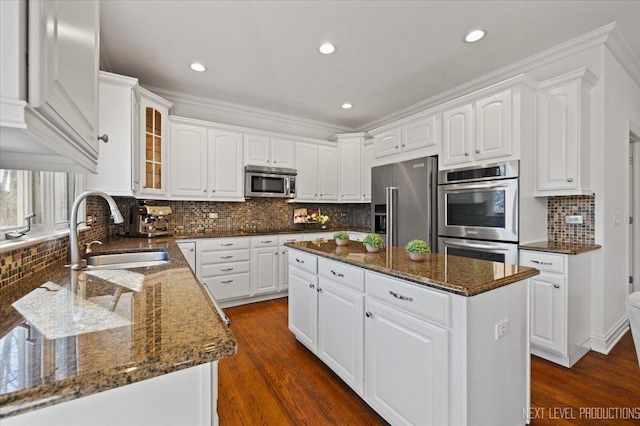 kitchen with dark stone countertops, a kitchen island, stainless steel appliances, a sink, and glass insert cabinets