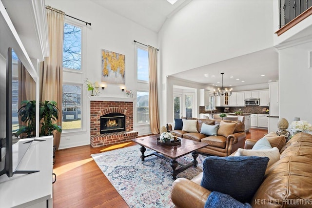 living room featuring a brick fireplace, a notable chandelier, light wood-type flooring, and high vaulted ceiling