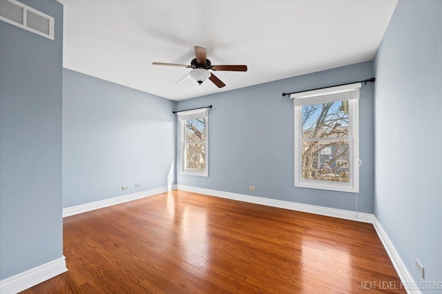 spare room with wood finished floors, baseboards, visible vents, and ceiling fan