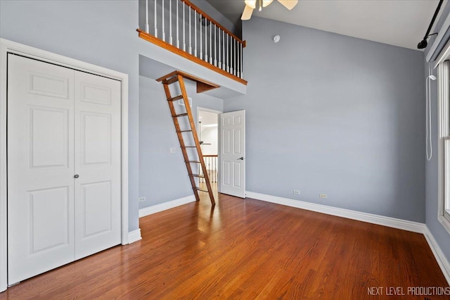 interior space with baseboards, a ceiling fan, wood finished floors, and a towering ceiling