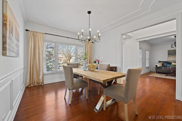 dining area featuring dark wood-style flooring, a decorative wall, an inviting chandelier, and ornamental molding