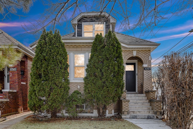 view of front of house featuring entry steps, brick siding, and roof with shingles