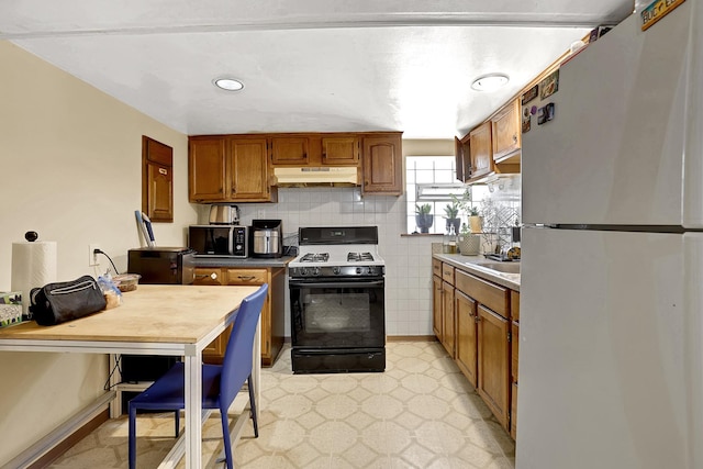 kitchen featuring range with gas stovetop, freestanding refrigerator, under cabinet range hood, stainless steel microwave, and brown cabinets