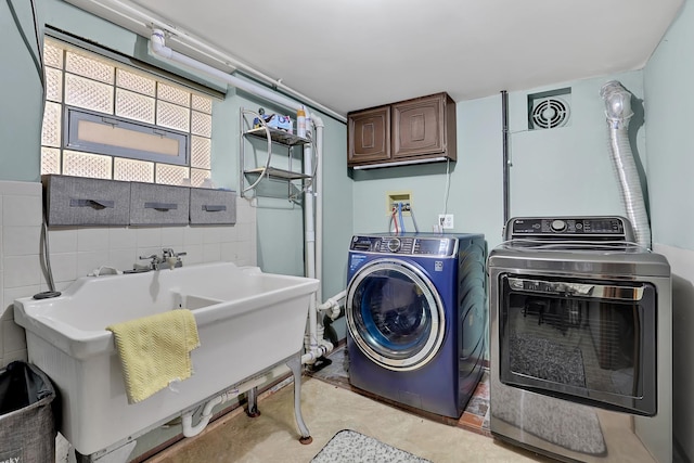 laundry area with visible vents, washer and dryer, cabinet space, tile walls, and a sink