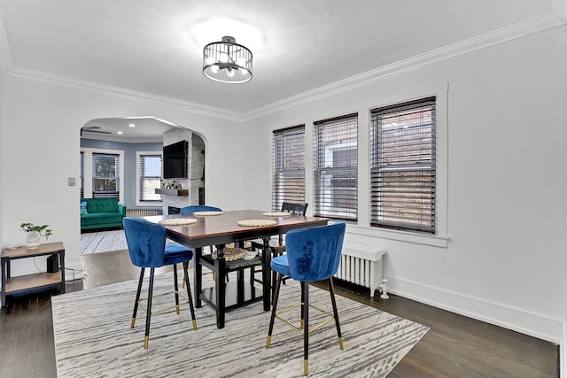 dining space featuring ornamental molding, wood finished floors, radiator heating unit, arched walkways, and baseboards