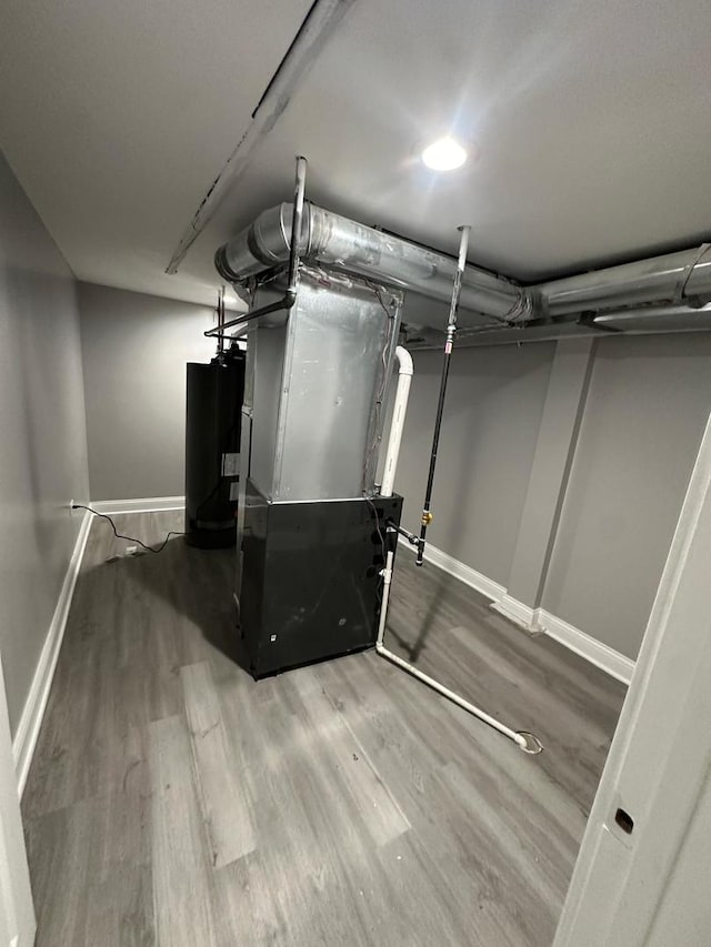 unfinished basement with heating unit, baseboards, wood finished floors, and water heater