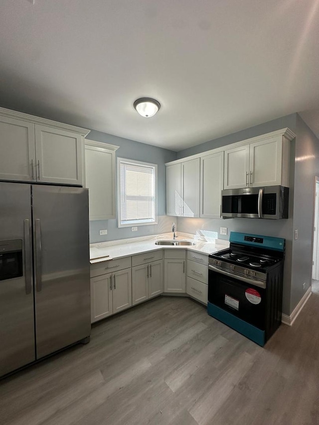 kitchen with baseboards, light wood-style flooring, a sink, light countertops, and appliances with stainless steel finishes