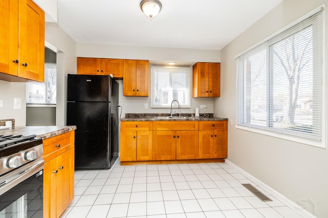 kitchen featuring baseboards, visible vents, stainless steel range with gas stovetop, freestanding refrigerator, and a sink