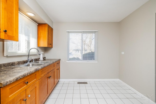 kitchen with a sink, baseboards, brown cabinets, and light tile patterned floors