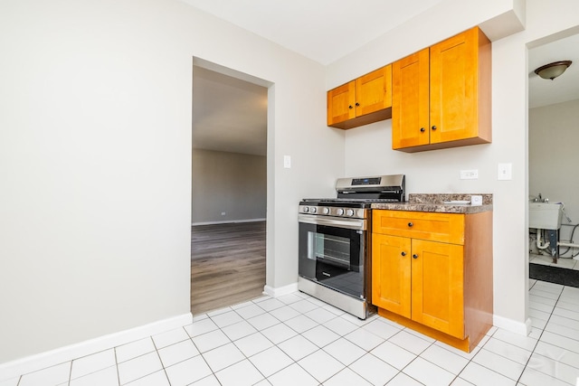 kitchen with light tile patterned floors, gas range, brown cabinets, and baseboards