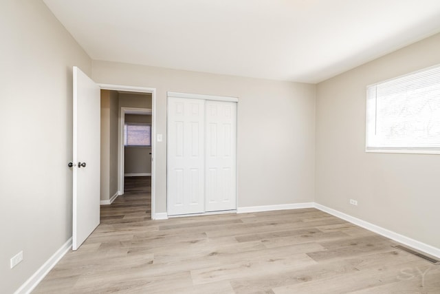 unfurnished bedroom featuring visible vents, baseboards, a closet, and light wood-style flooring