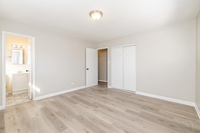 unfurnished bedroom featuring a closet, baseboards, ensuite bath, and light wood-style flooring