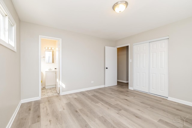 unfurnished bedroom with baseboards, light wood-type flooring, a closet, and connected bathroom