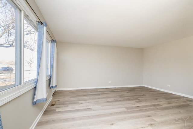 empty room with light wood-style floors, visible vents, and baseboards