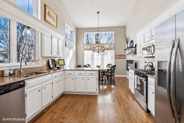 kitchen with stone counters, wood finished floors, white cabinets, stainless steel appliances, and a sink