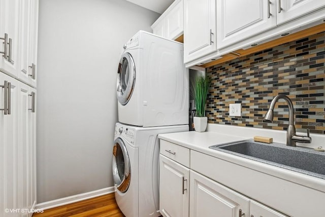 laundry area featuring baseboards, stacked washer and dryer, wood finished floors, cabinet space, and a sink