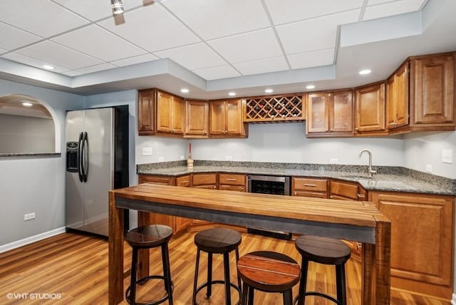 kitchen with a tray ceiling, wine cooler, brown cabinetry, and stainless steel fridge