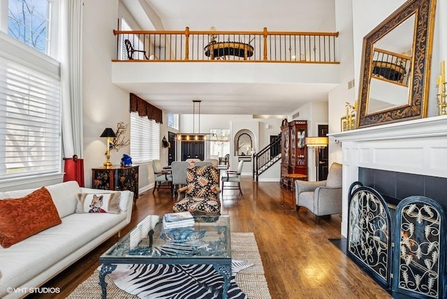 living area featuring stairway, wood finished floors, baseboards, a high ceiling, and a tile fireplace