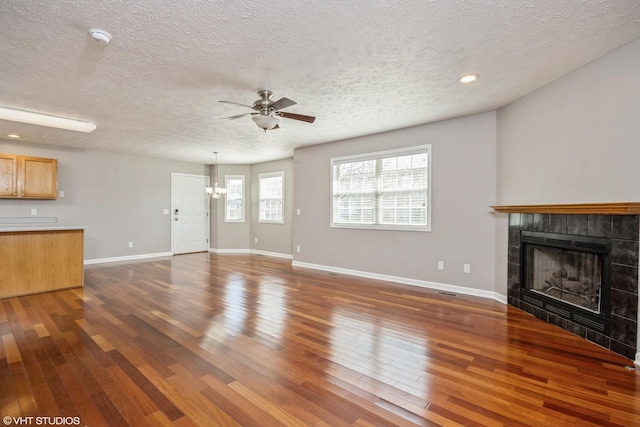 unfurnished living room featuring ceiling fan with notable chandelier, a textured ceiling, wood finished floors, a fireplace, and baseboards