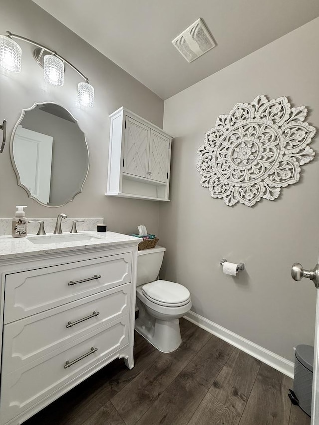 half bathroom with visible vents, toilet, wood finished floors, baseboards, and vanity