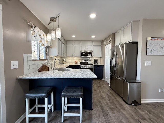 kitchen with dark wood finished floors, a peninsula, a sink, appliances with stainless steel finishes, and backsplash