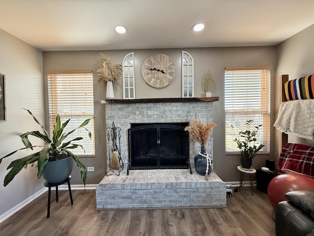 living area featuring plenty of natural light, a brick fireplace, baseboards, and wood finished floors