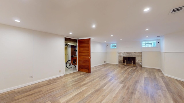 below grade area featuring visible vents, baseboards, recessed lighting, a stone fireplace, and light wood-style floors