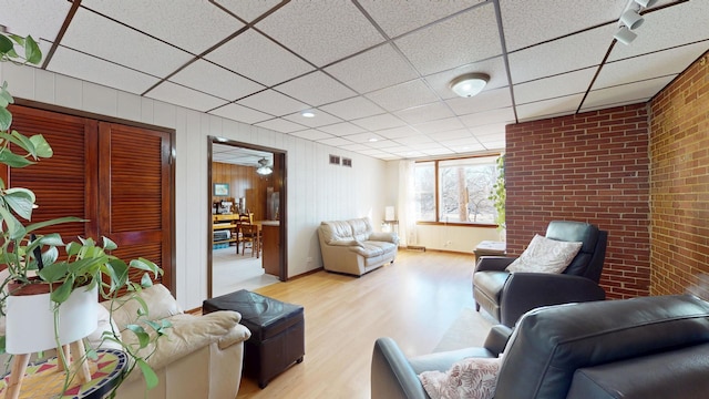 living room with wood finished floors, visible vents, brick wall, and a paneled ceiling