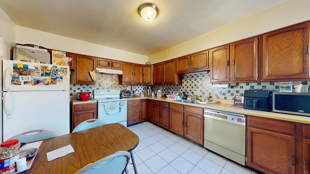 kitchen with tasteful backsplash, under cabinet range hood, light countertops, white appliances, and a sink