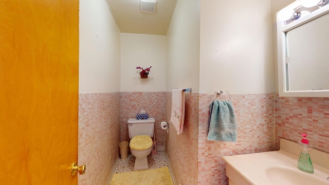 half bath with visible vents, a wainscoted wall, toilet, tile patterned floors, and tile walls