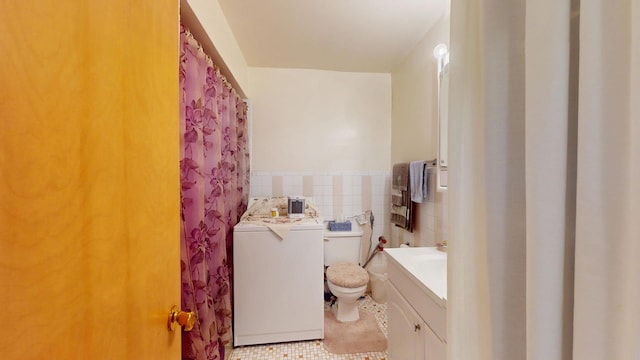 full bath with a wainscoted wall, toilet, tile walls, washer / dryer, and vanity