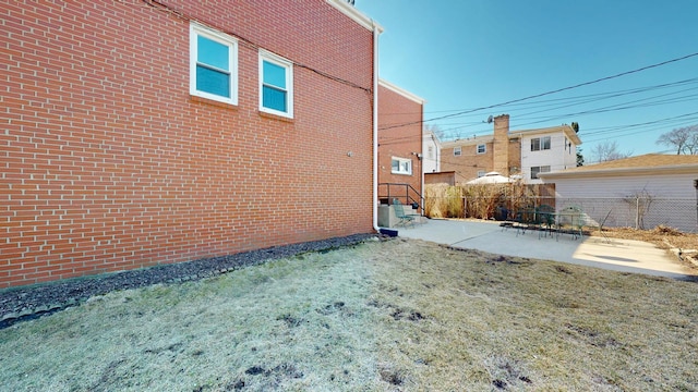 view of side of property featuring a patio area, brick siding, and fence