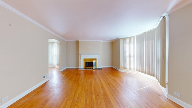 unfurnished living room featuring light wood finished floors, crown molding, baseboards, arched walkways, and a glass covered fireplace