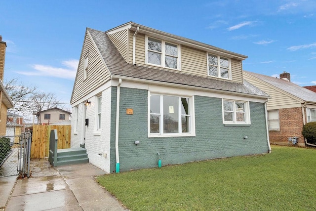 view of front of home featuring brick siding, a shingled roof, a front lawn, and fence