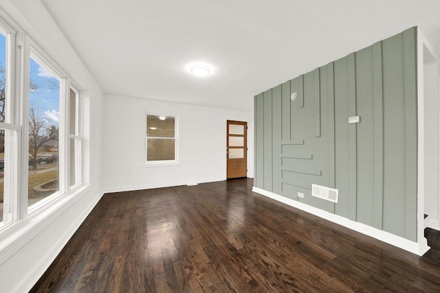 empty room featuring visible vents, baseboards, and dark wood-style flooring