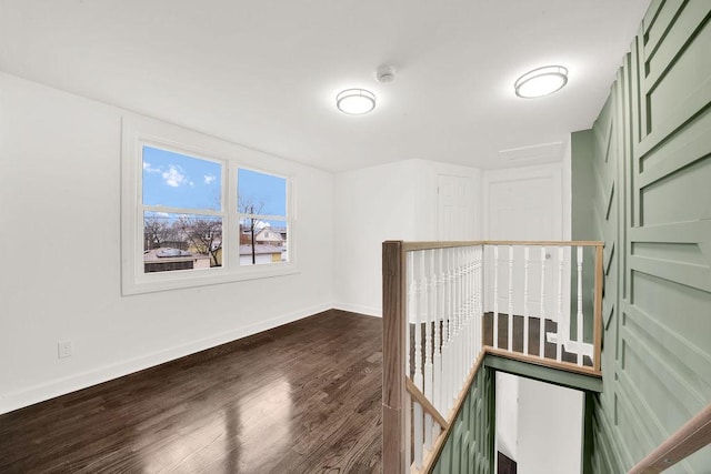 corridor featuring an upstairs landing, dark wood-style flooring, and baseboards