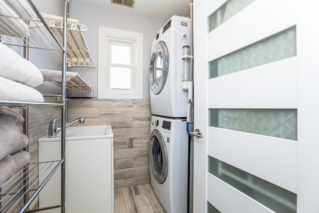 laundry room featuring visible vents, stacked washing maching and dryer, laundry area, a sink, and light wood-style floors