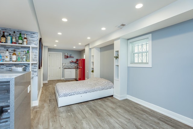 unfurnished bedroom with visible vents, baseboards, light wood-type flooring, recessed lighting, and a bar