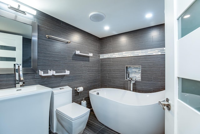 full bathroom with tile walls, a freestanding tub, and toilet