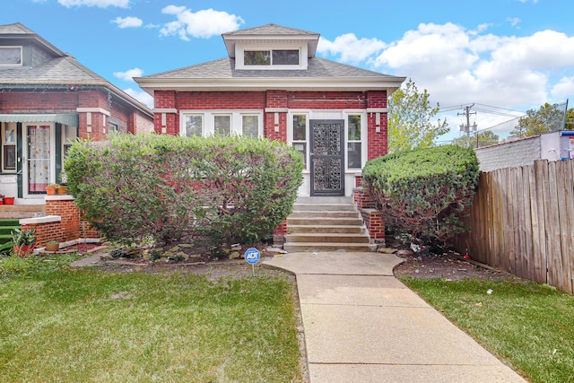 view of front of property featuring brick siding, a shingled roof, a front yard, and fence