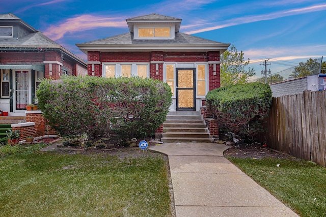 view of front facade with entry steps, fence, roof with shingles, a front yard, and brick siding