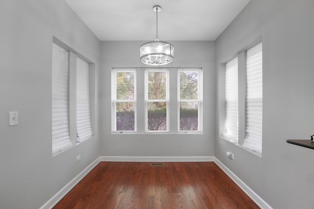 unfurnished dining area with a notable chandelier, baseboards, and wood finished floors