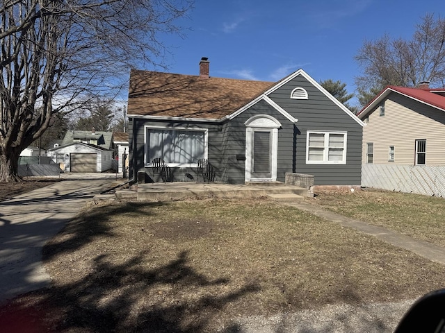 bungalow-style house featuring an outbuilding, driveway, a detached garage, fence, and a chimney